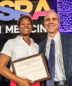Picture of Tobi Hunter holding a plaque, posting with President Steven Cohen